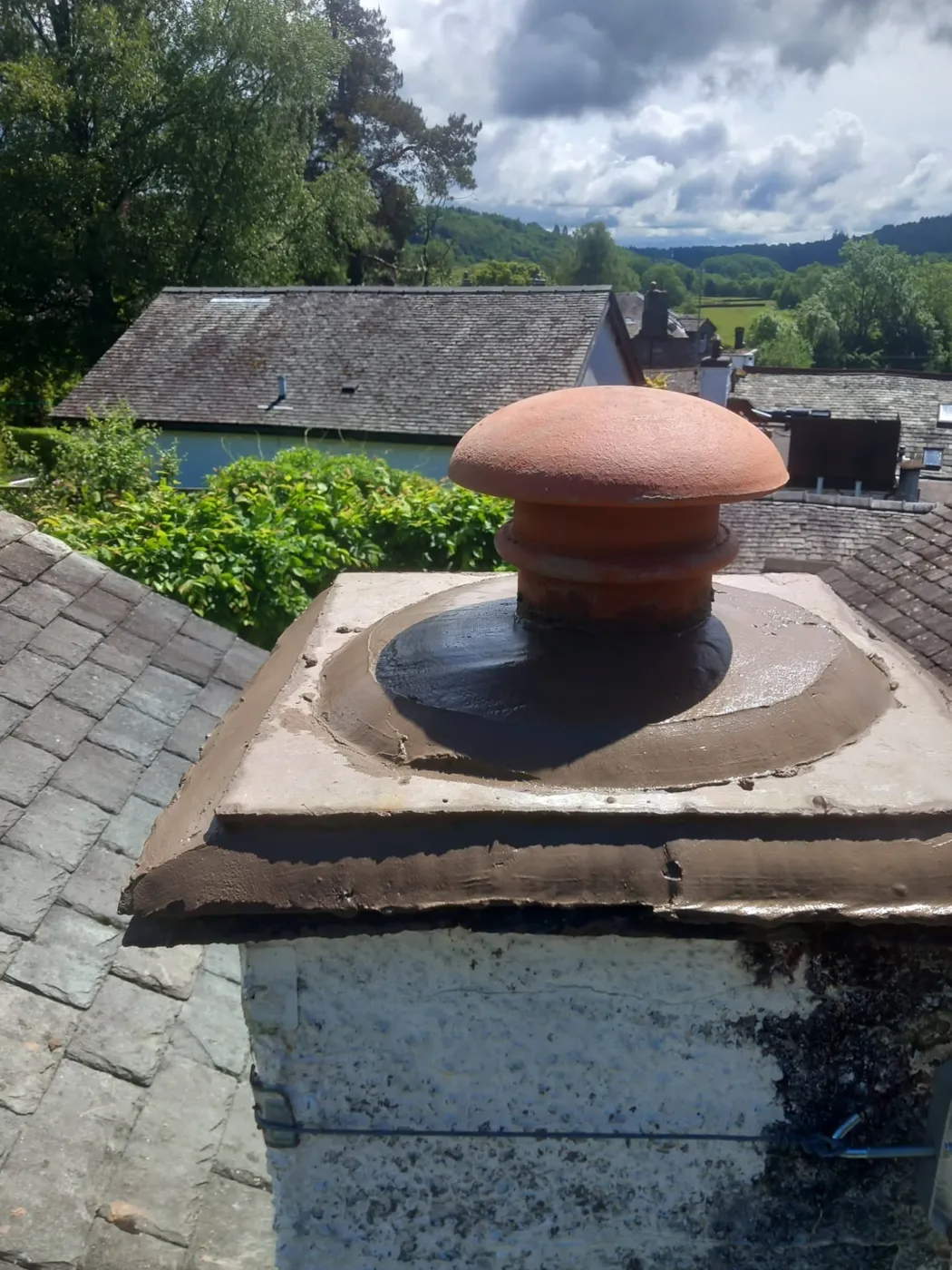Terracotta chimney pot with fresh mortar on a rendered stack, Lake District hills behind